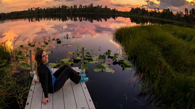 A person sitting on a dock on the edge of a lake.